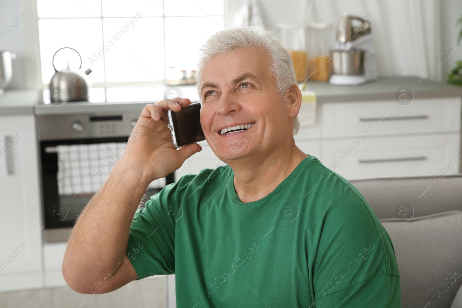 Photo of Mature man laughing while talking on phone at home