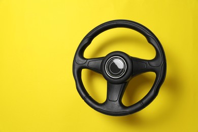Photo of New black steering wheel on yellow background, space for text