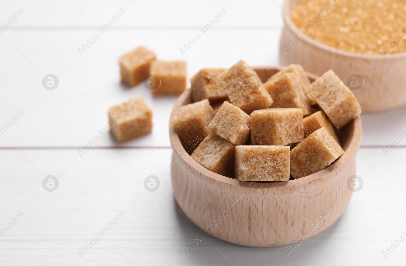 Photo of Brown sugar cubes in bowl on white wooden table, closeup. Space for text