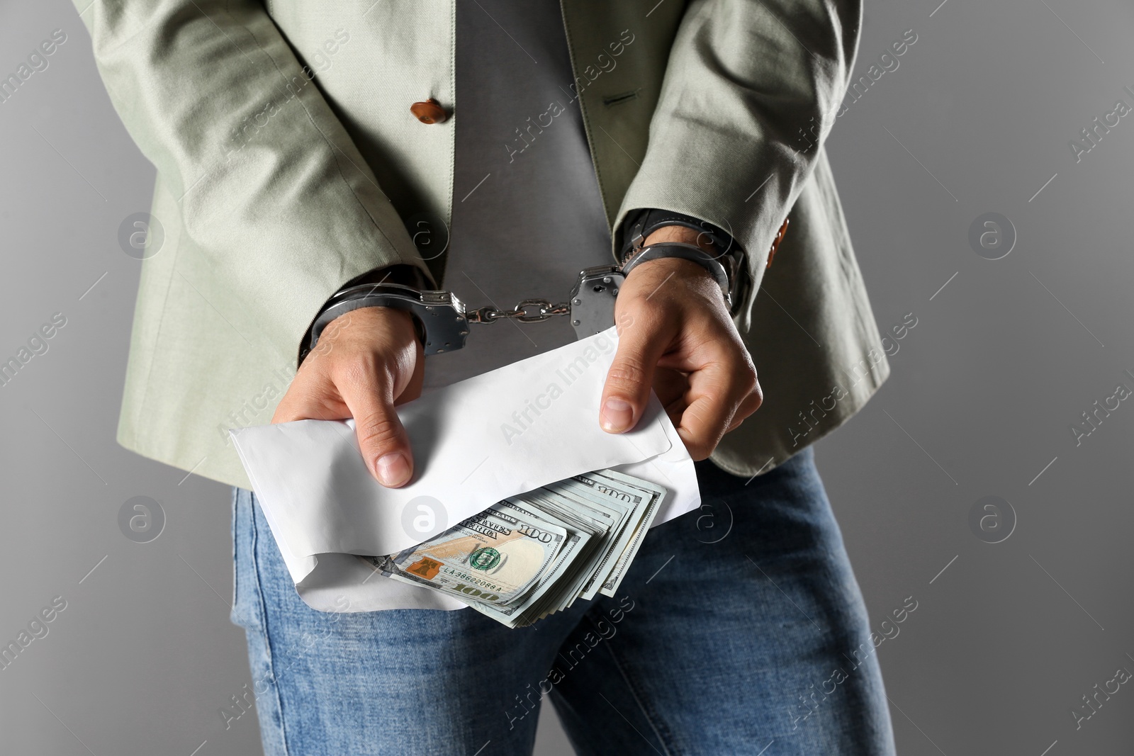 Photo of Man in handcuffs holding bribe money on grey background, closeup