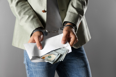 Photo of Man in handcuffs holding bribe money on grey background, closeup