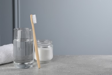 Photo of Bamboo toothbrush, glass of water and jar of baking soda on light grey table, space for text