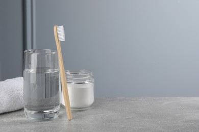 Bamboo toothbrush, glass of water and jar of baking soda on light grey table, space for text