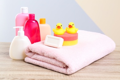 Photo of Baby cosmetic products, toys and towel on table against color background