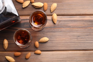 Photo of Liqueur glasses with tasty amaretto and almonds on wooden table, flat lay. Space for text