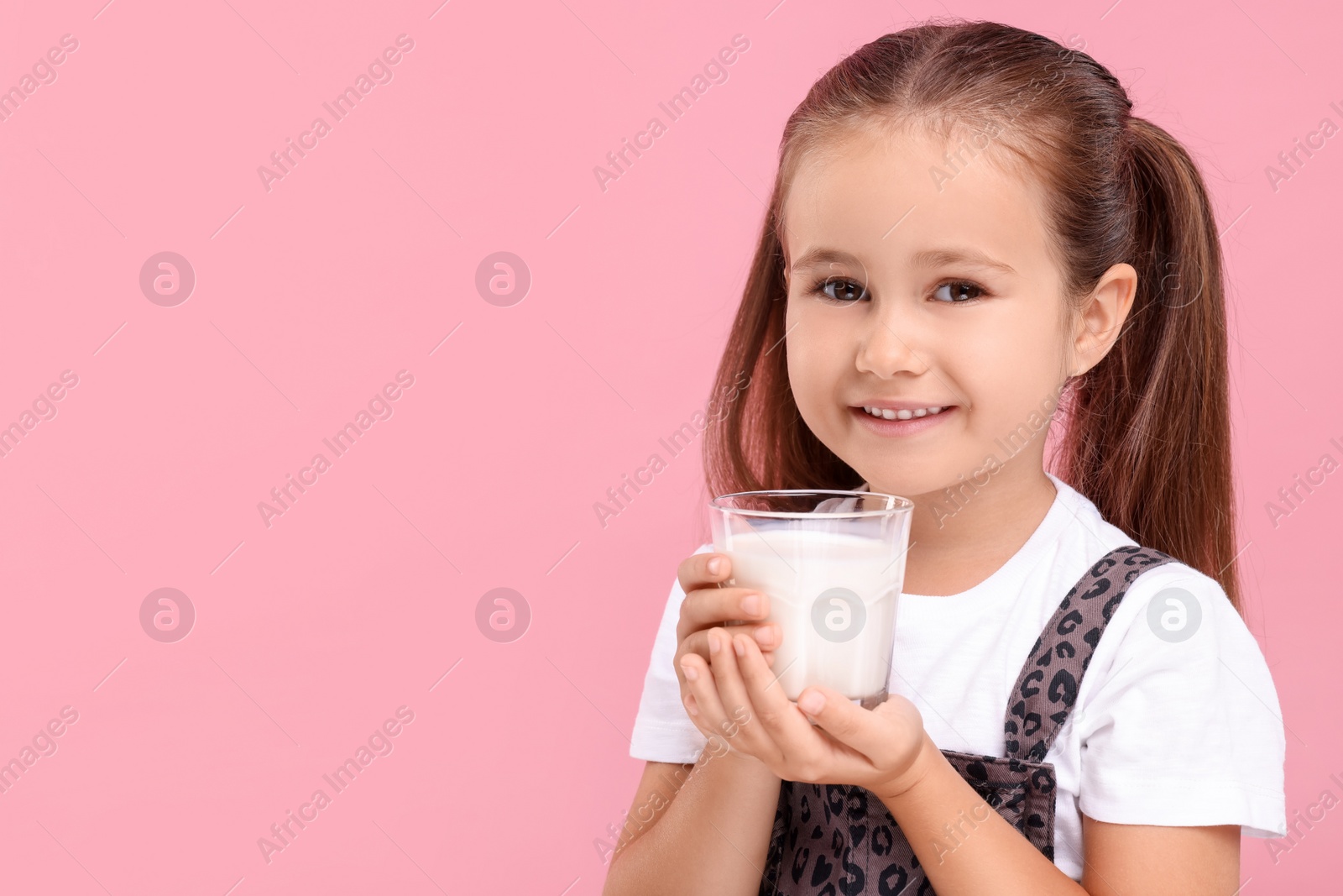 Photo of Cute girl with glass of fresh milk on pink background, space for text