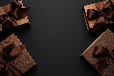 Brown gift boxes decorated with satin bows on black background, flat lay. Space for text