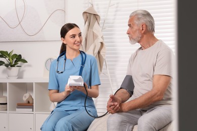 Young healthcare worker measuring senior man's blood pressure indoors