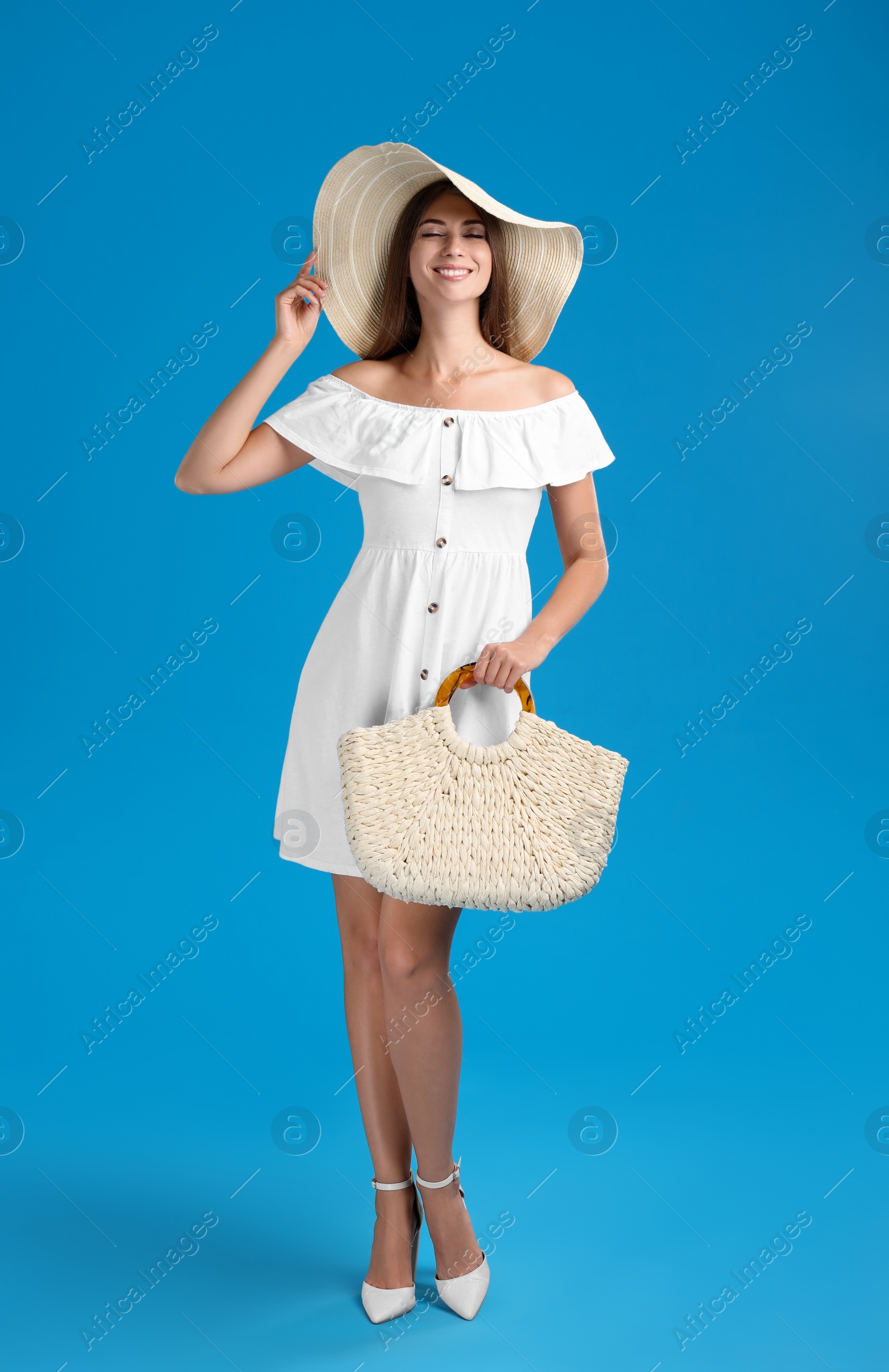 Photo of Beautiful young woman with stylish straw bag on light blue background