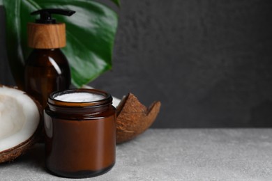 Photo of Jar of hand cream and coconut pieces on grey table, space for text