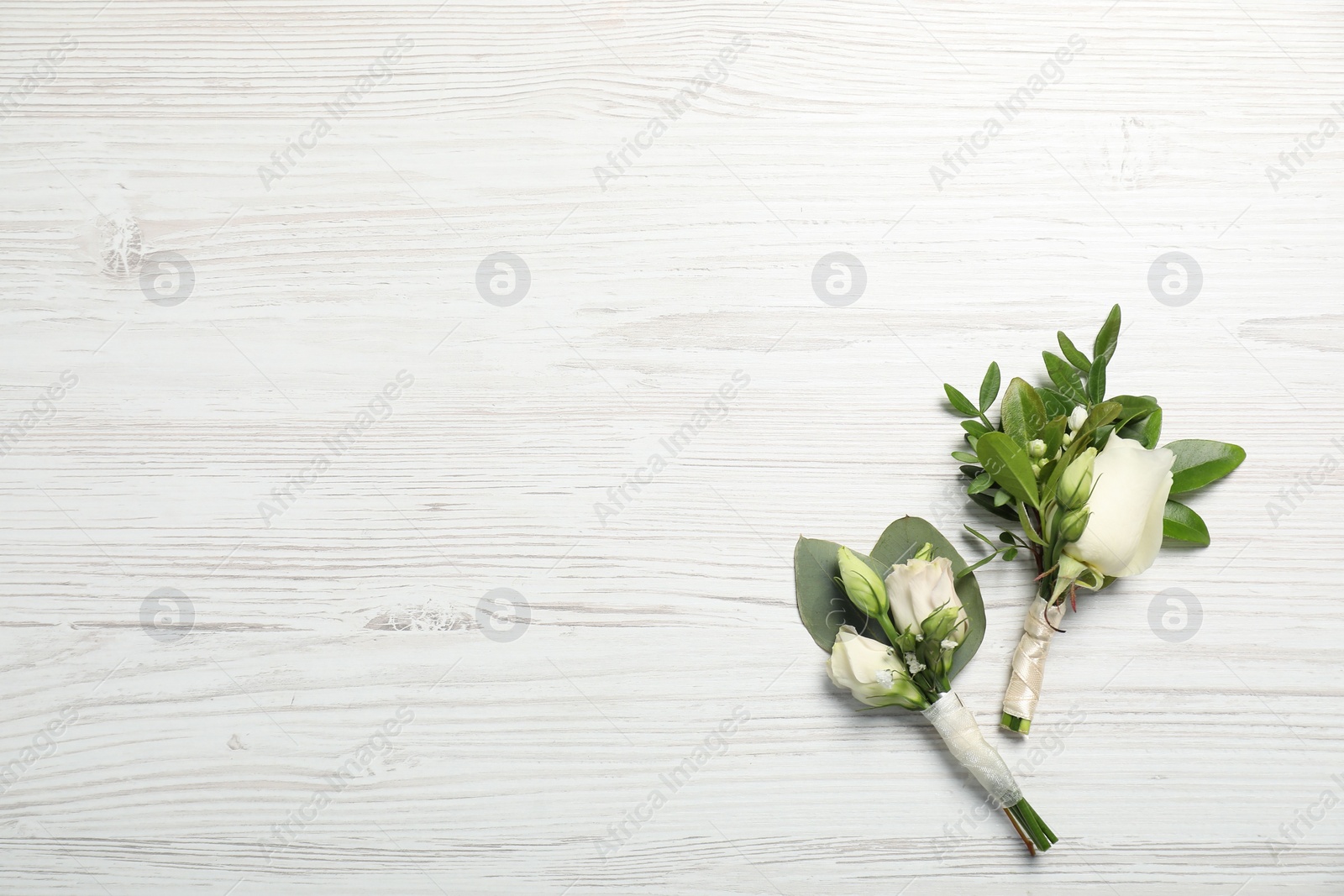 Photo of Wedding stuff. Stylish boutonnieres on white wooden table, top view. Space for text