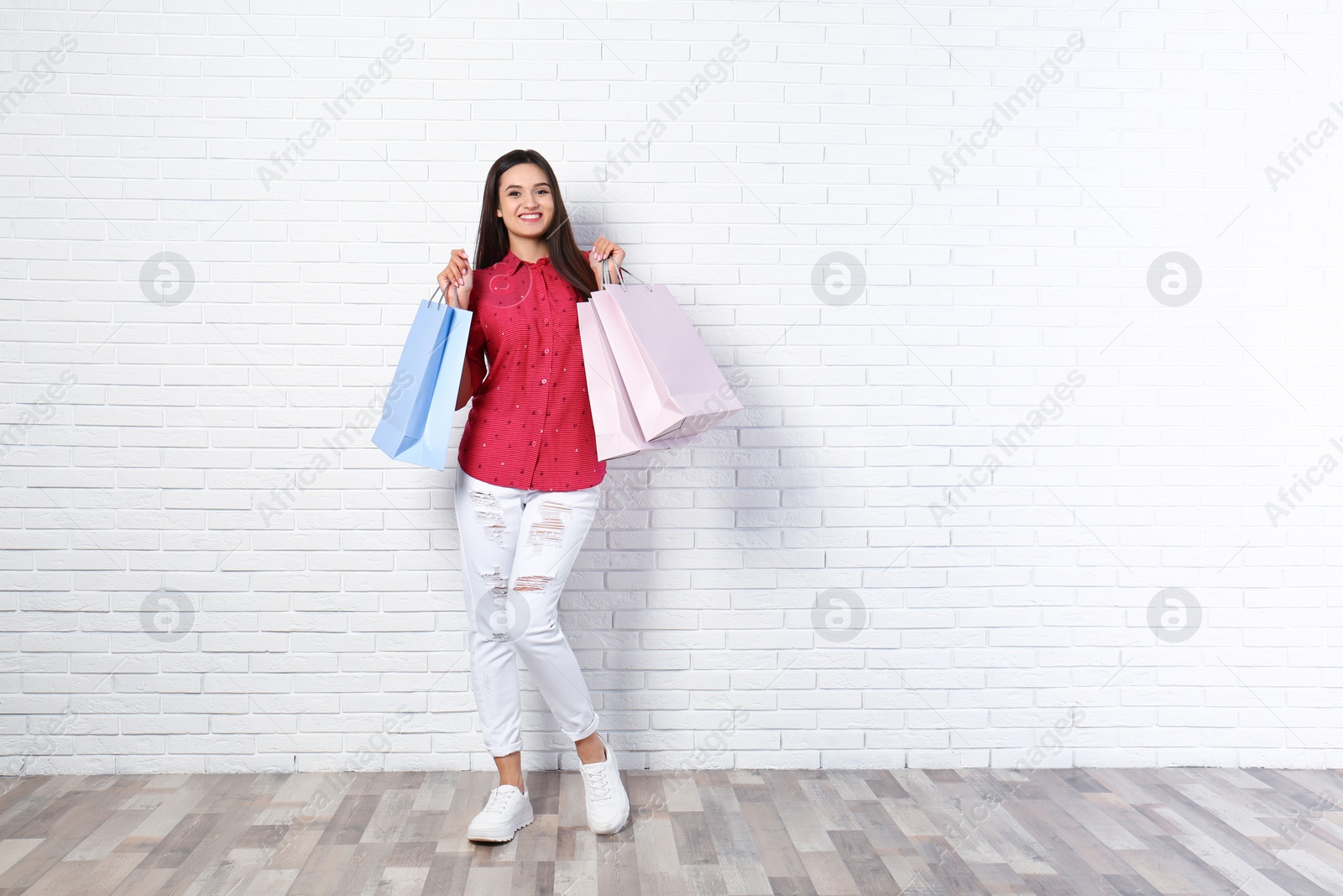 Photo of Beautiful young woman with blank paper bags near brick wall, space for text