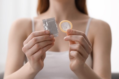 Photo of Woman holding unwrapped condom indoors, closeup. Safe sex