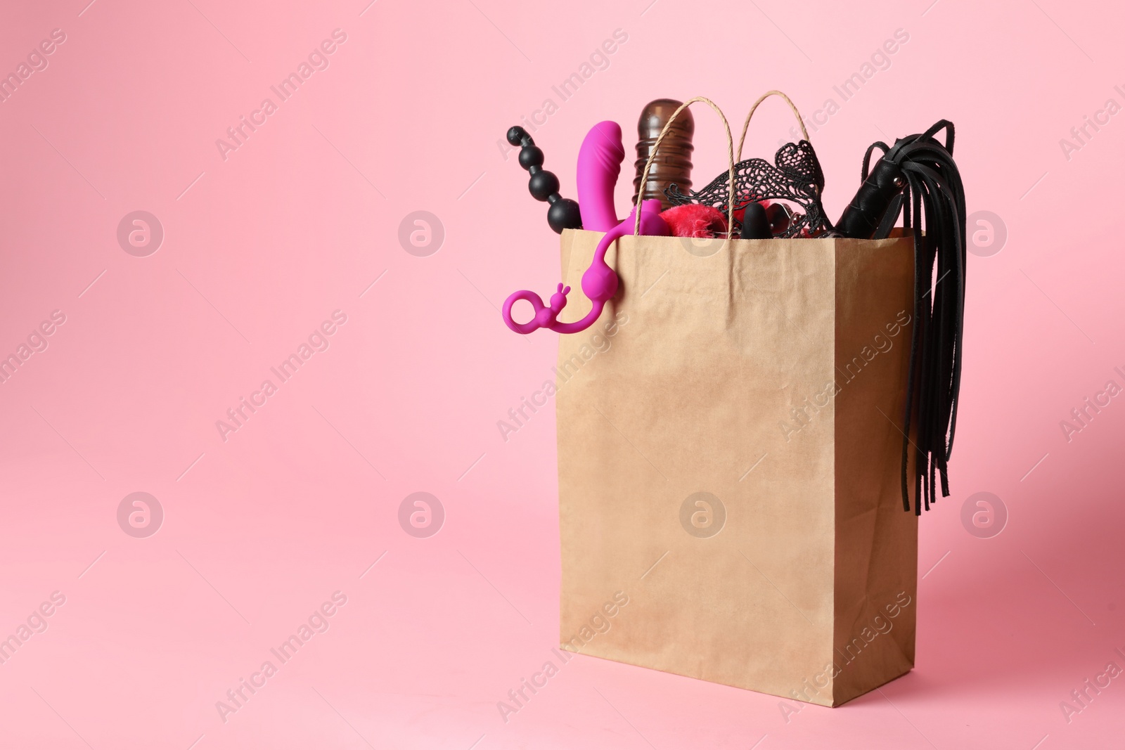 Photo of Paper shopping bag with different sex toys on pink background. Space for text