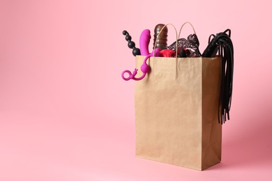 Paper shopping bag with different sex toys on pink background. Space for text