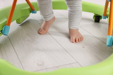 Photo of Cute little boy making first steps with baby walker on wooden floor, closeup
