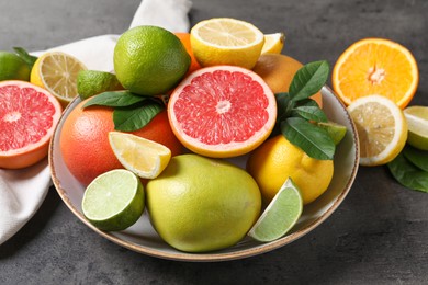 Photo of Different fresh citrus fruits and leaves on grey textured table, closeup