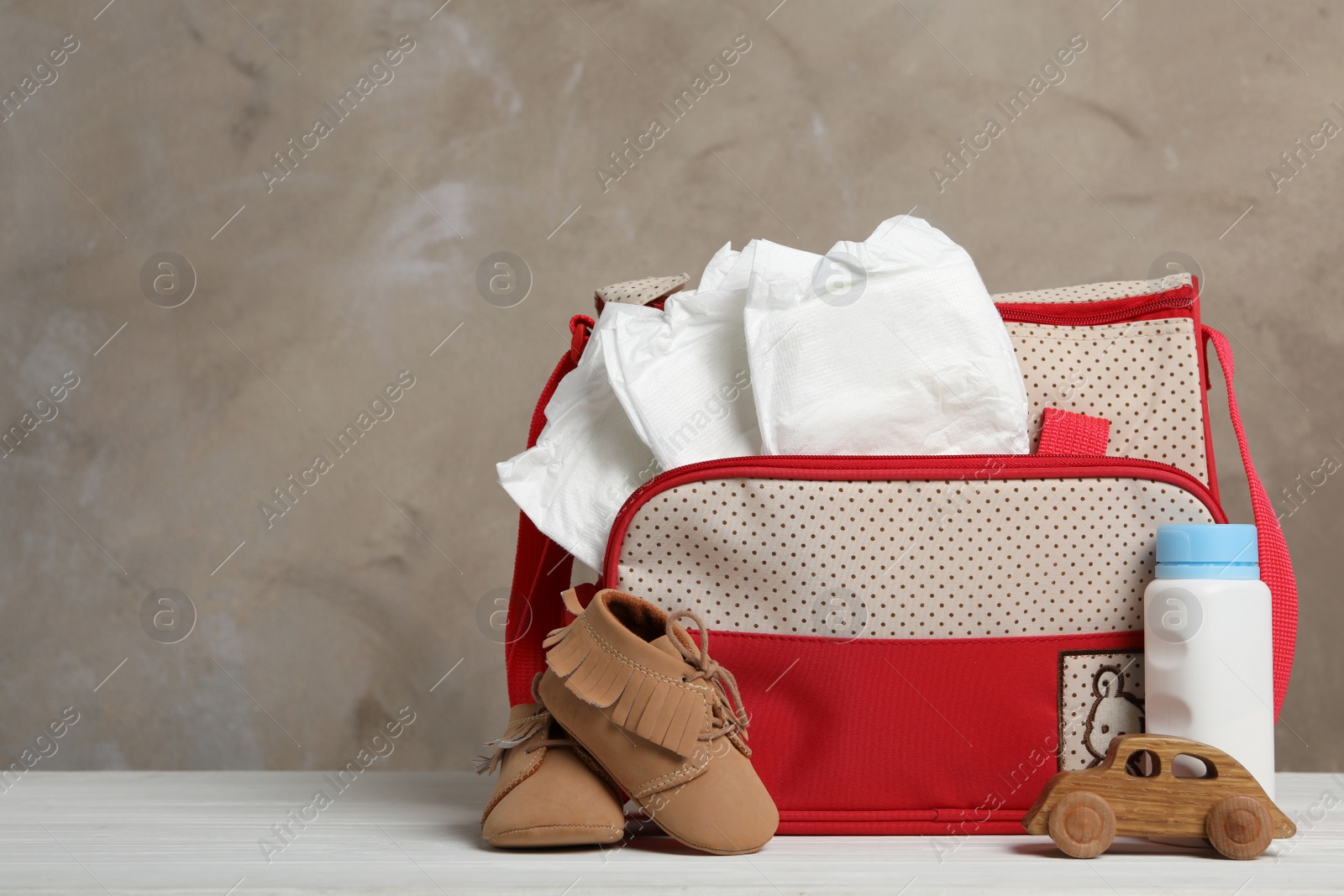 Photo of Bag with diapers and baby accessories on white wooden table. Space for text