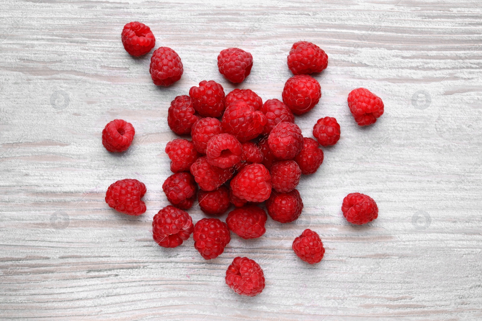Photo of Tasty ripe raspberries on white wooden table, flat lay