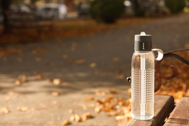 Sport bottle of water on wooden bench in park, space for text