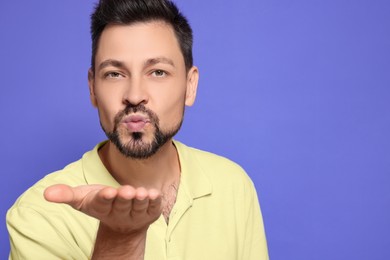 Handsome man blowing kiss on violet background. Space for text