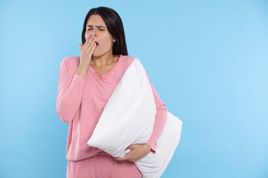 Photo of Sleepy young woman with soft pillow yawning on light blue background, space for text