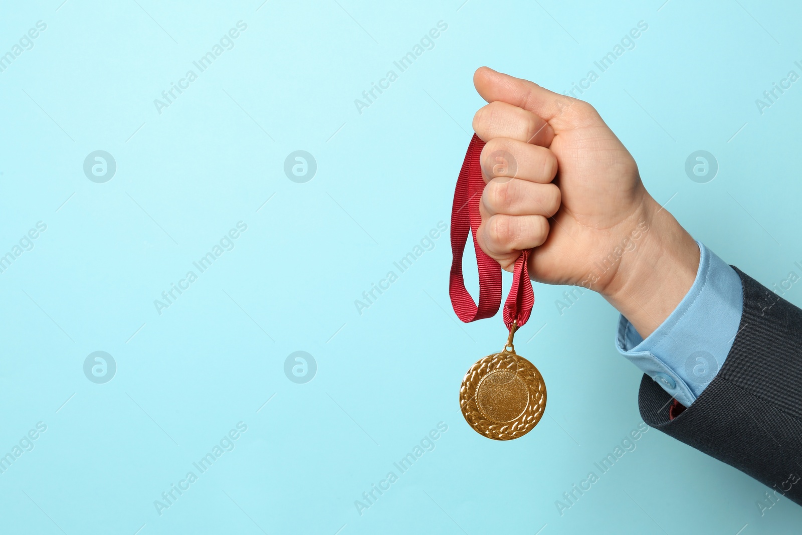 Photo of Man holding golden medal on color background, closeup. Space for text