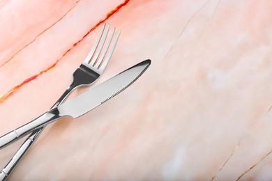 Photo of Shiny fork and knife on pink marble table, closeup. Space for text