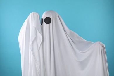 Photo of Creepy ghost. Person covered with white sheet on light blue background