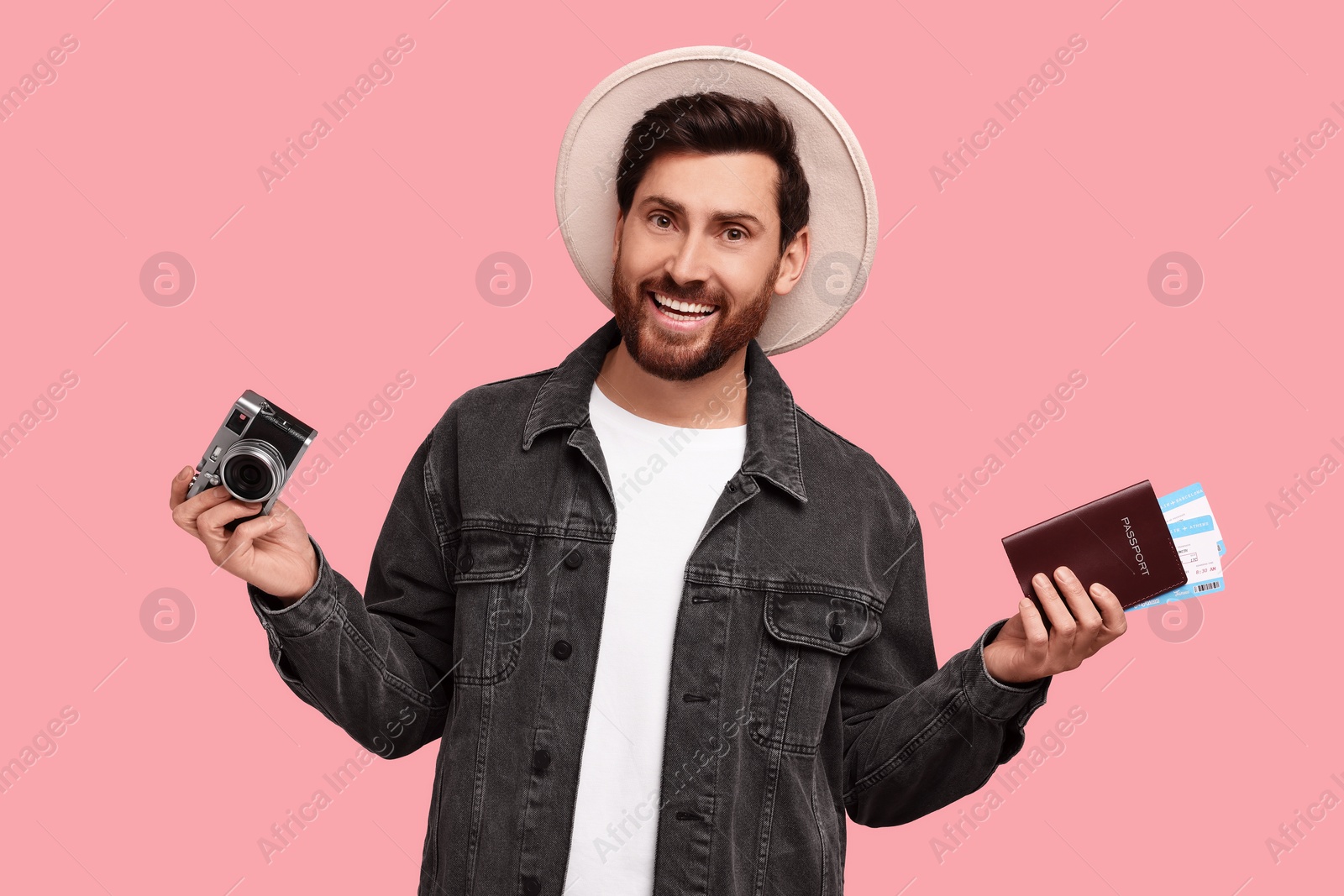 Photo of Smiling man with passport, tickets and camera on pink background