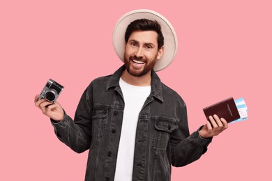 Smiling man with passport, tickets and camera on pink background