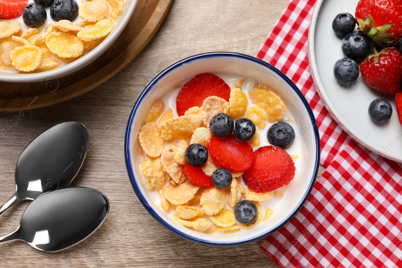 Photo of Delicious crispy cornflakes with milk and fresh berries on wooden table, flat lay