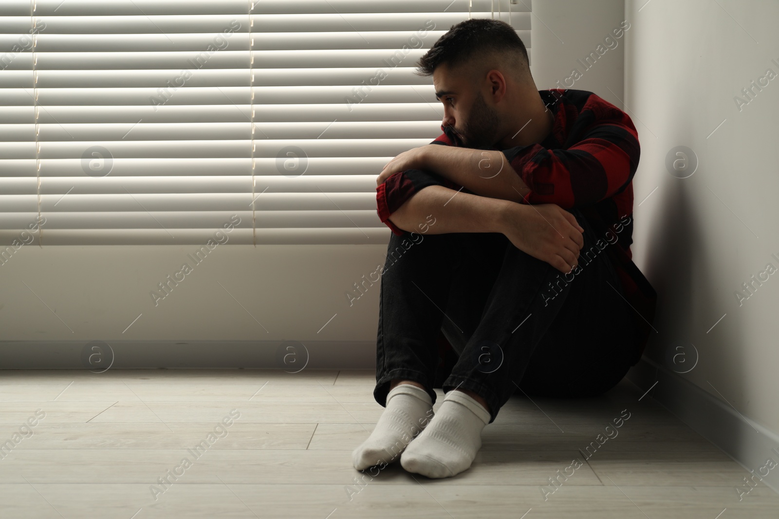 Photo of Sad man sitting on floor at home. Space for text