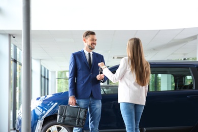 Photo of Salesperson giving car key to man in auto dealership