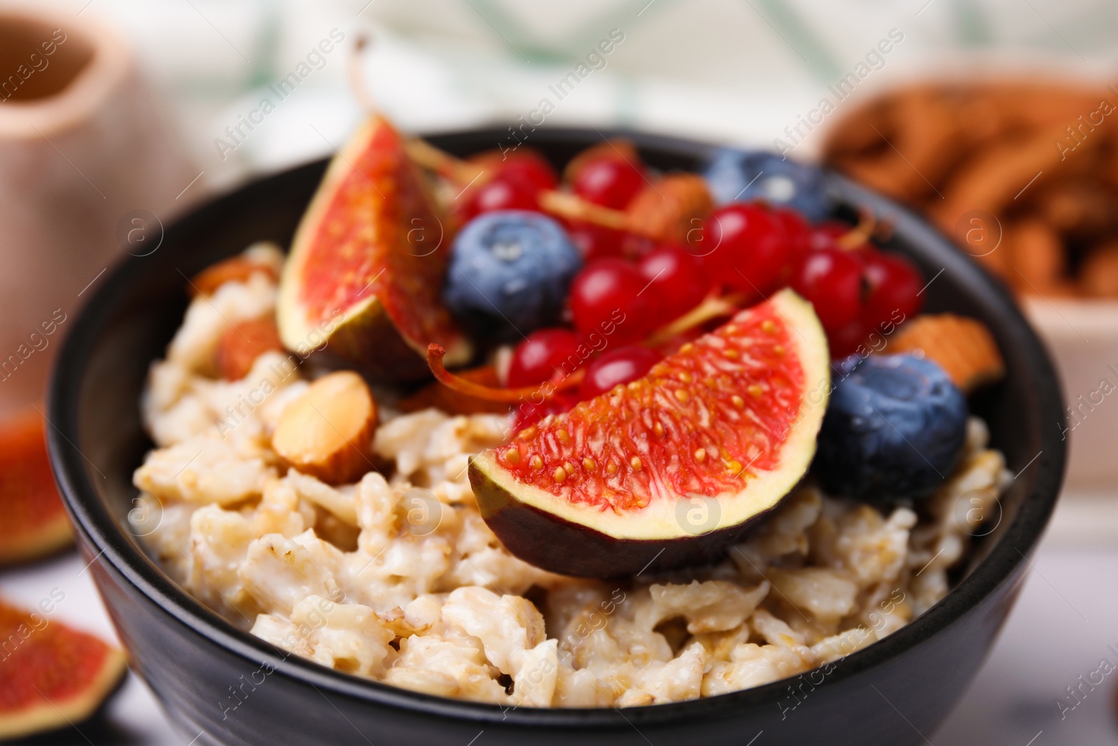 Photo of Bowl of oatmeal with berries, almonds and fig pieces on table, closeup