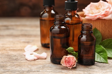 Photo of Bottles of rose essential oil and flowers on wooden table, space for text