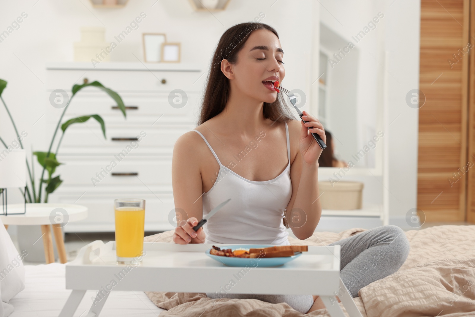 Photo of Happy young woman having breakfast on bed at home