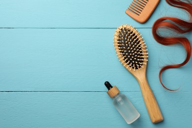 Photo of Brush, comb, bottle of essential oil and red hair strand on light blue wooden table, flat lay. Space for text