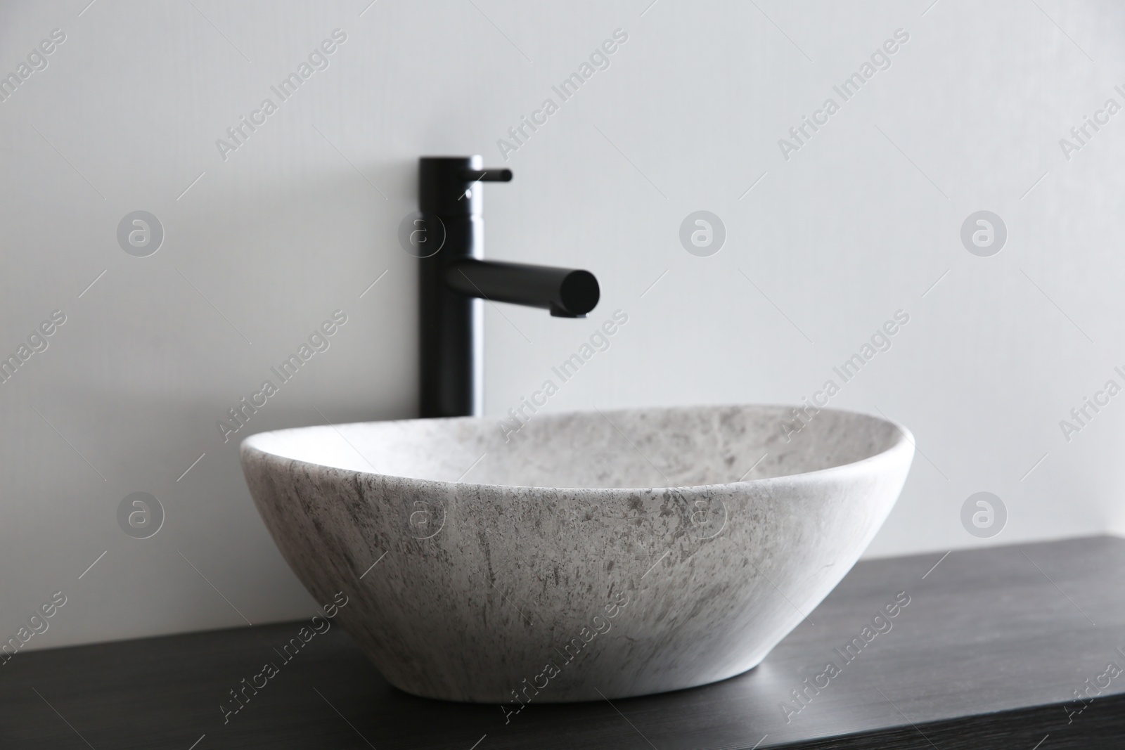 Photo of Stone vessel sink with faucet on wooden countertop