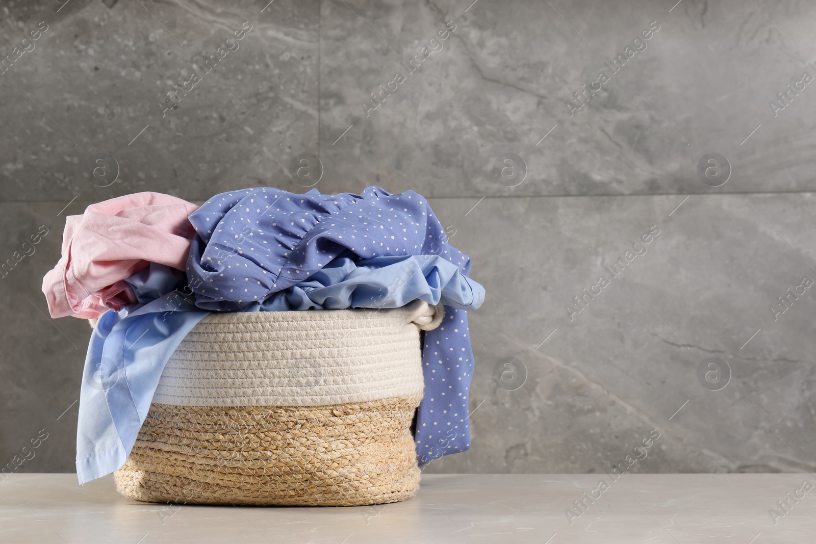 Photo of Laundry basket with clothes near grey wall. Space for text