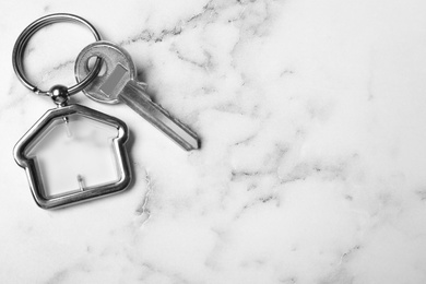 Photo of Key with trinket in shape of house on white marble background, top view and space for text. Real estate agent services