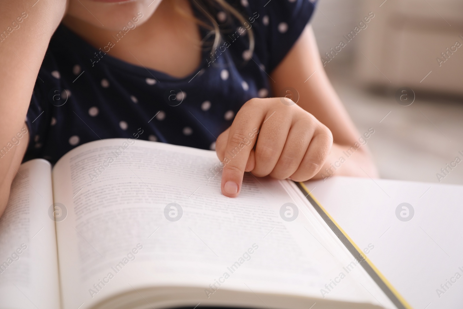 Photo of Cute little girl with book doing homework at table, closeup