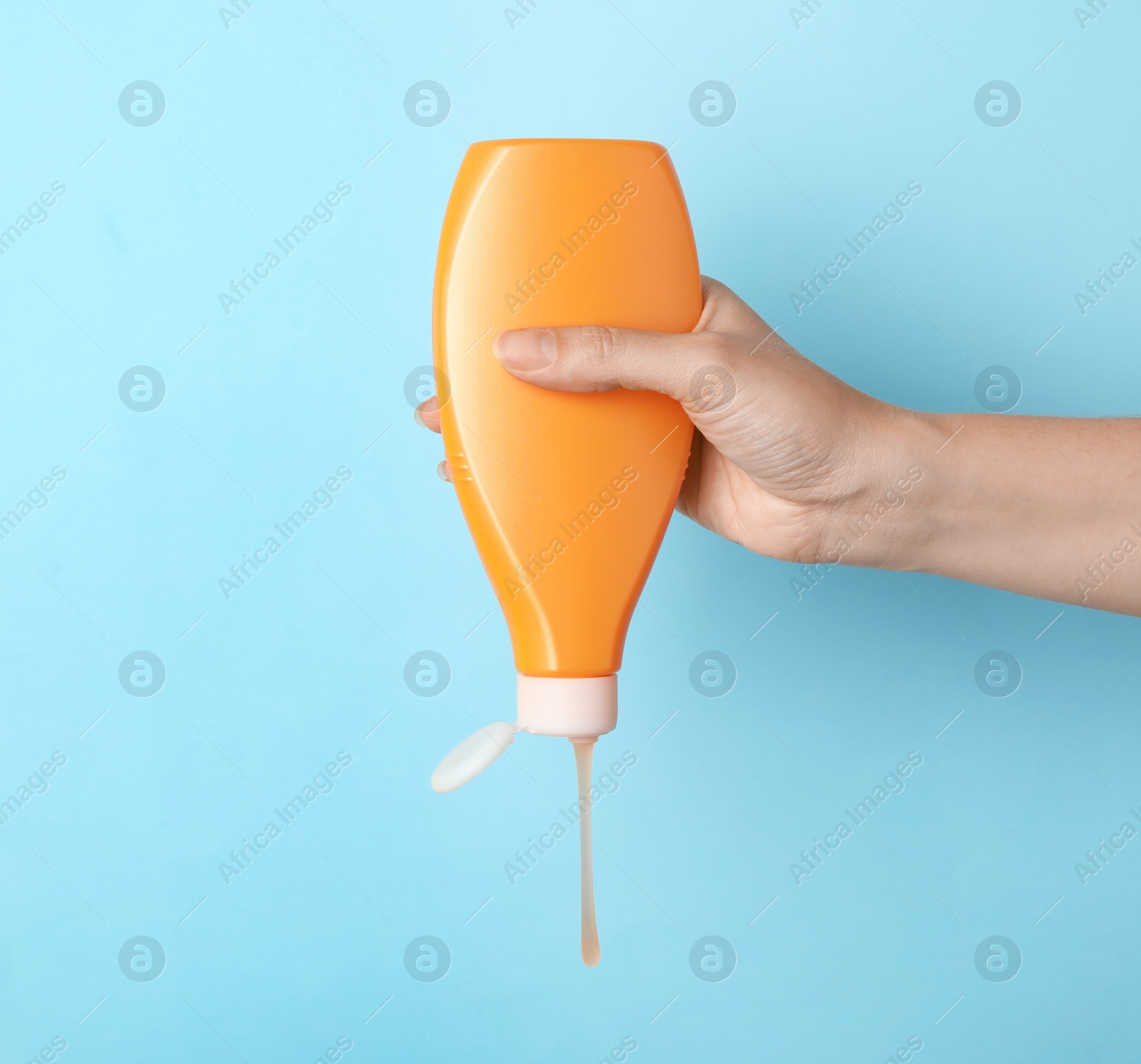 Photo of Woman pouring cosmetic product from bottle on color background, closeup. Space for text