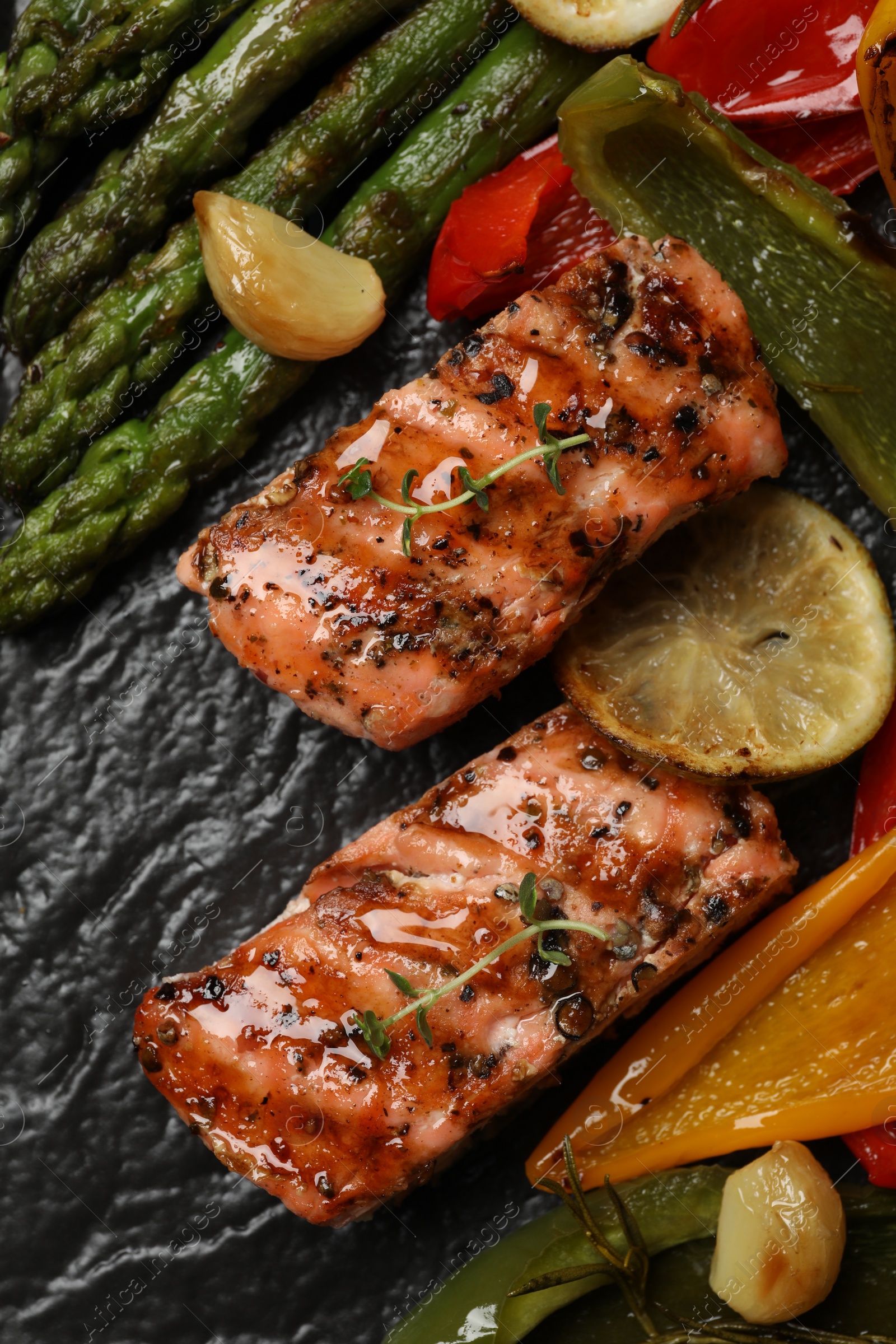 Photo of Tasty grilled salmon with lemon and vegetables on black slate, top view