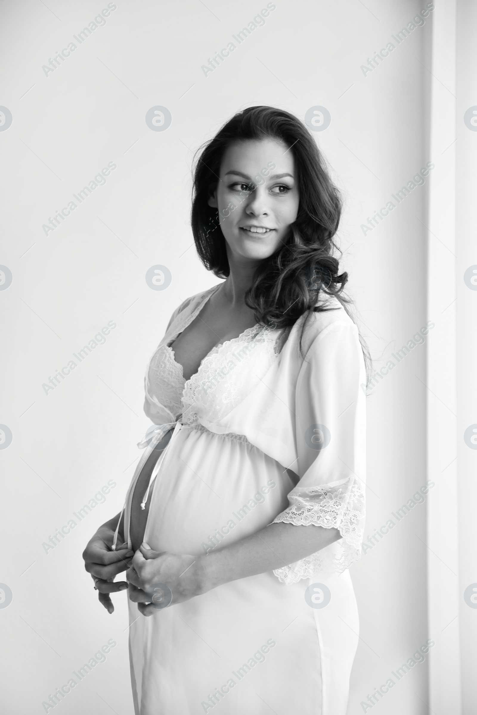 Photo of Young pregnant woman in lace nightgown on light background, black and white effect