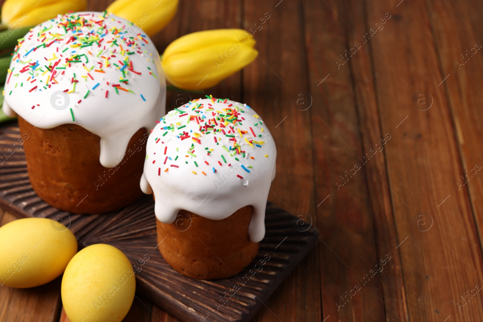 Photo of Tasty Easter cakes, decorated eggs and flowers on wooden table. Space for text