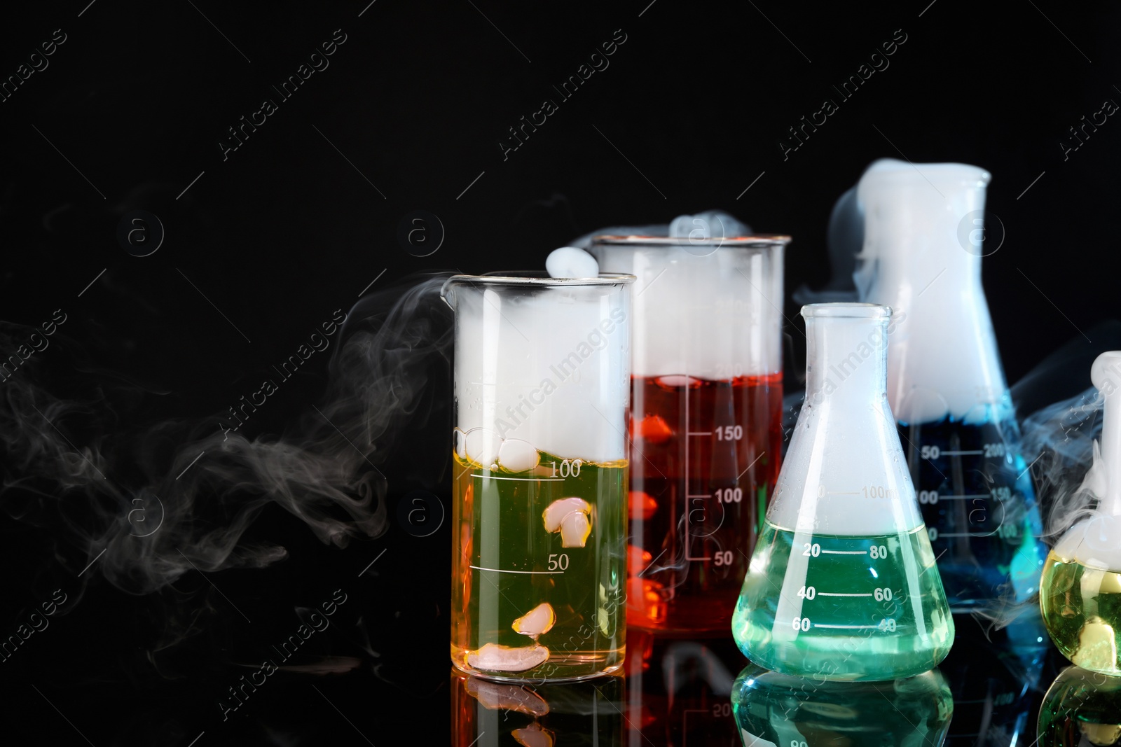 Photo of Laboratory glassware with colorful liquids and steam on black background. Chemical reaction