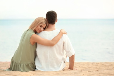 Photo of Happy romantic couple sitting together on beach, space for text