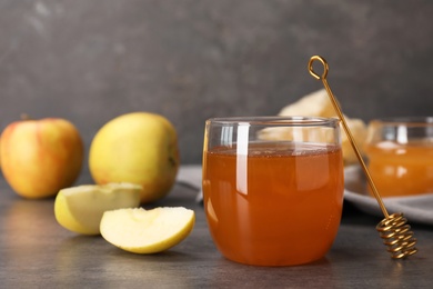 Photo of Glass of honey, apples and dipper on dark table