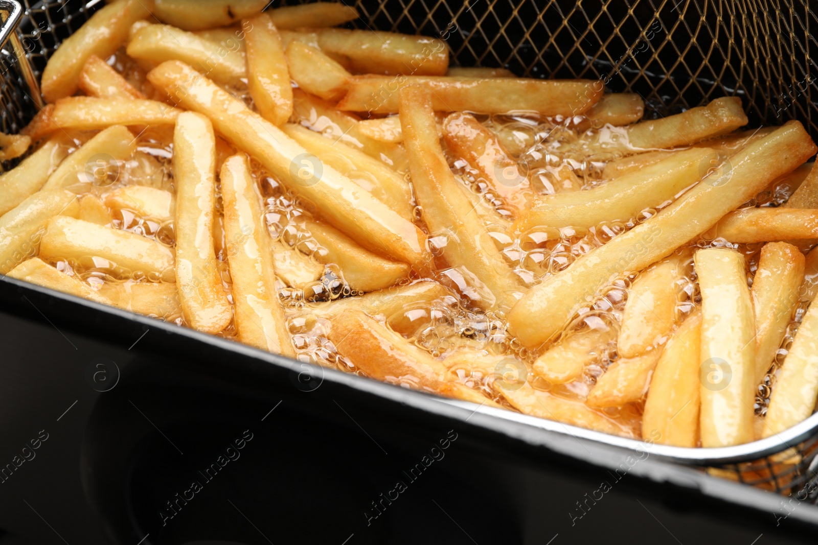 Photo of Cooking delicious french fries in hot oil, closeup